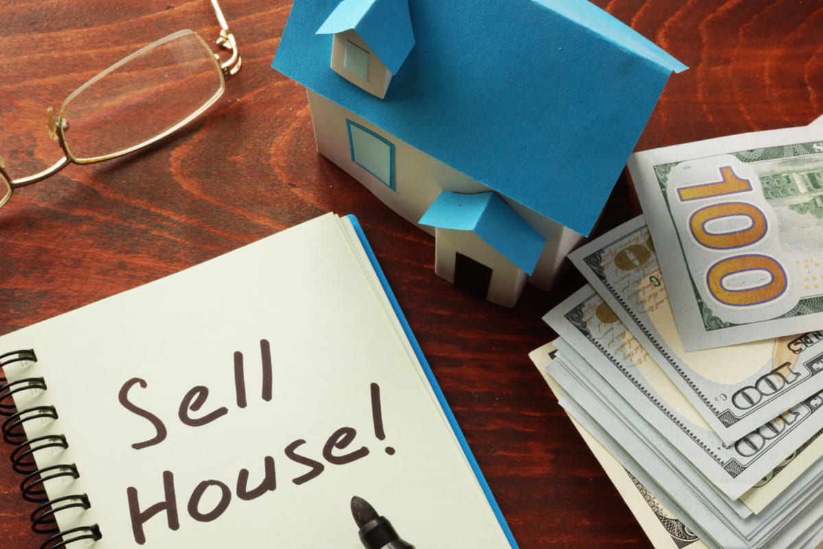 A house next to cash and a notebook that says Sell House!, buy my house for cash concept property evaluation